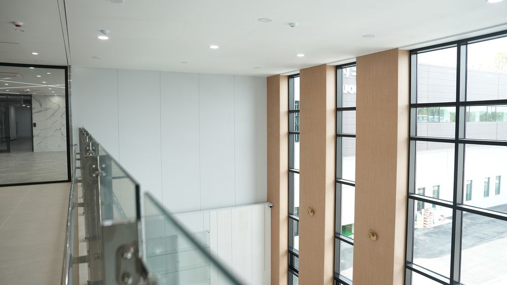 Double-height hall with white wall panels, oak-clad window piers and a glass balustrade on the mezzanine