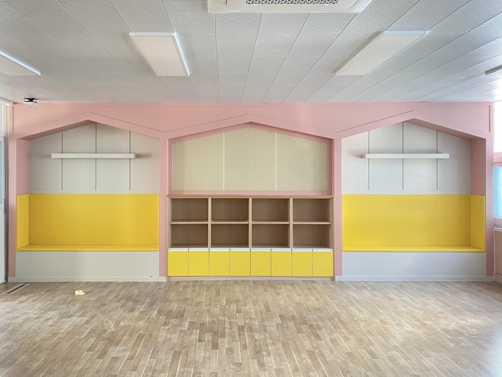 Classroom storage wall finished in yellow and pink pastel film, with the built-in shelving left open