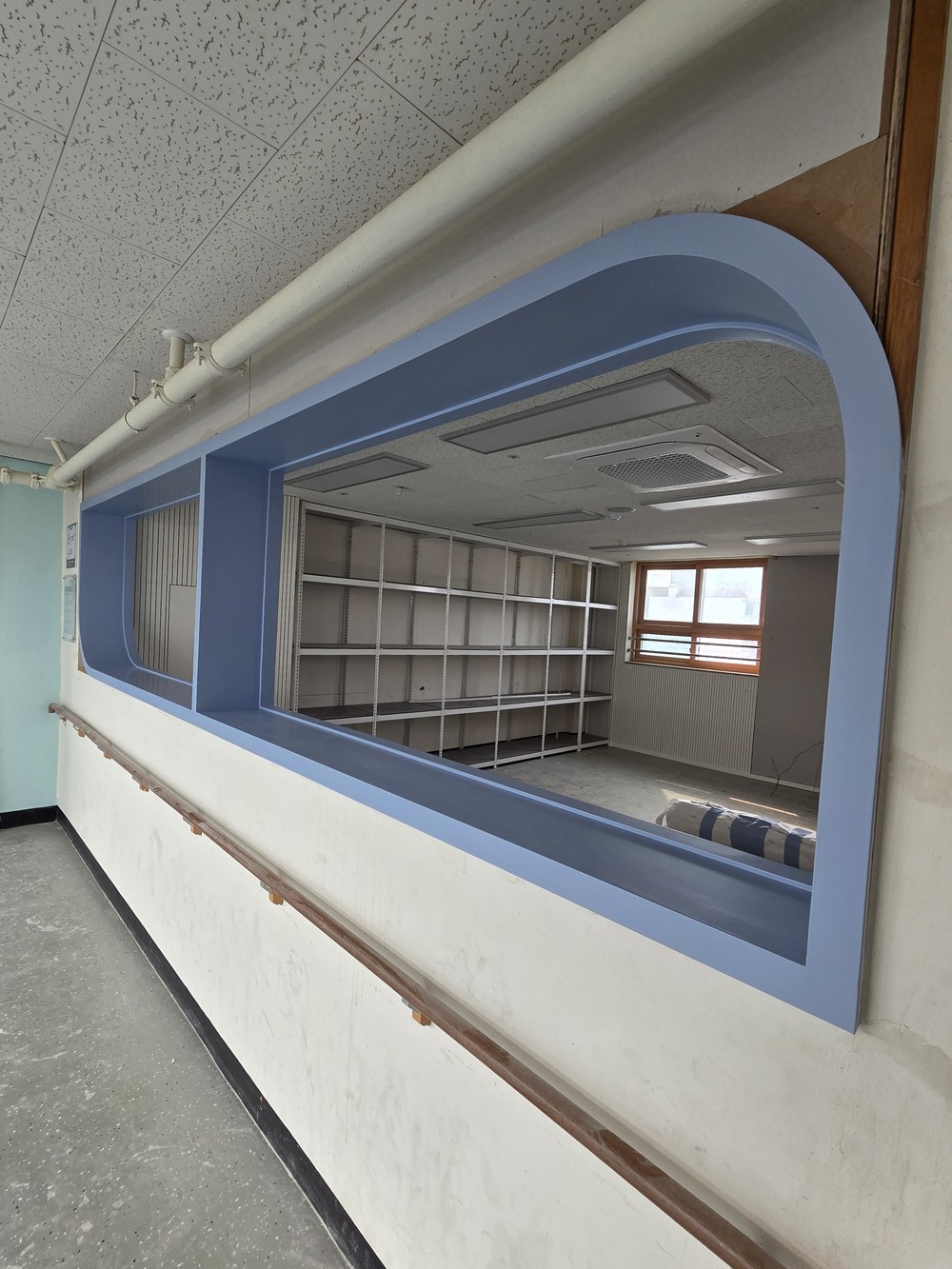 Corridor with a rounded interior window framed in blue film, a wooden handrail below it