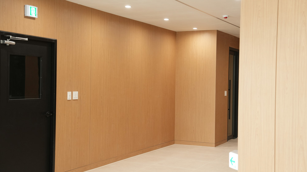 Corridor with oak-clad walls on both sides, a dark door with a vision panel and an exit sign above it
