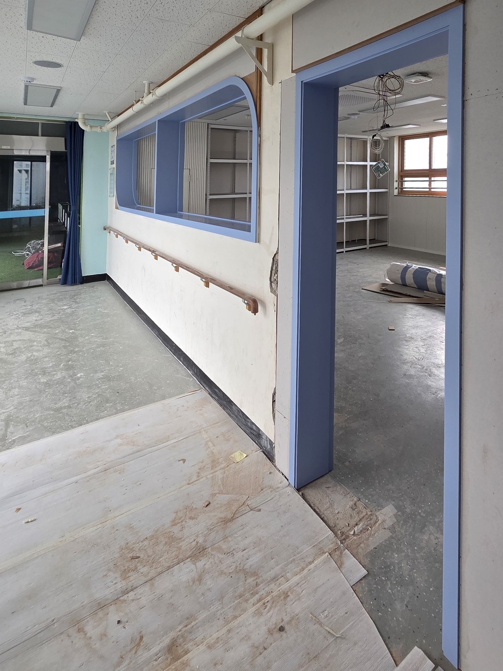 Mid-project view of an interior window and a door opening already framed in blue film, the corridor floor still bare