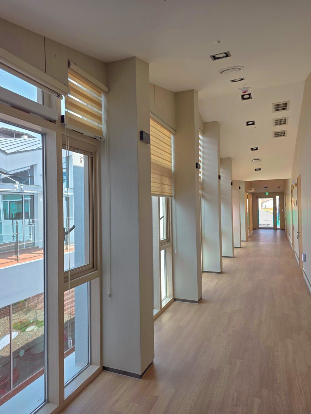 Sunlit corridor with tall windows, pale wall piers and a wood floor