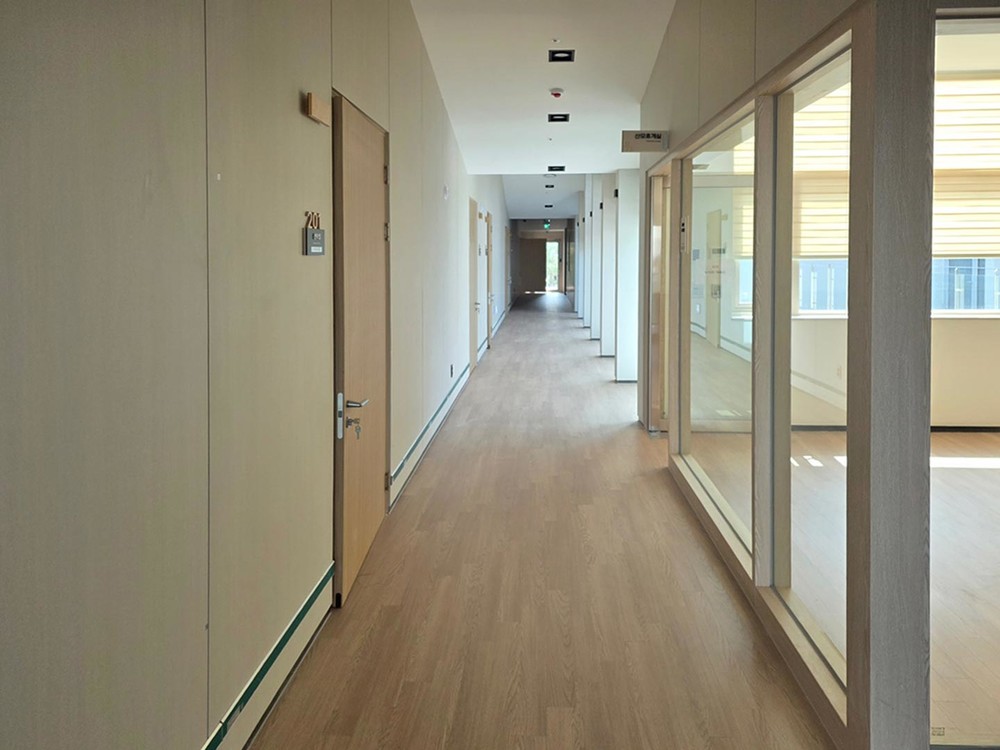 Corridor with oak doors carrying room numbers, pale walls and a glazed partition into a room