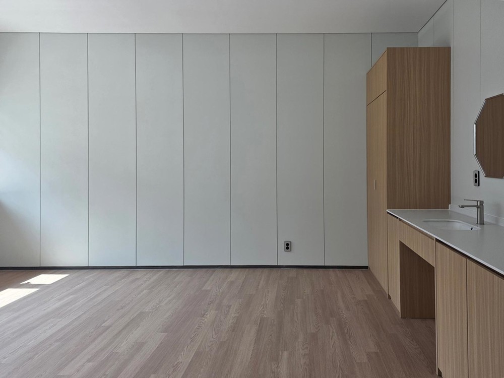 Patient room with a full-height white panelled wall and an oak cabinet and vanity unit at the end